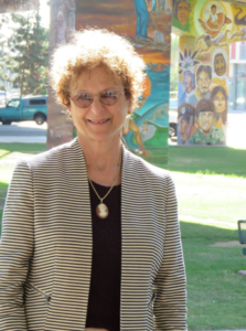 Smiling woman in glasses and striped jacket standing outdoors near colorful murals