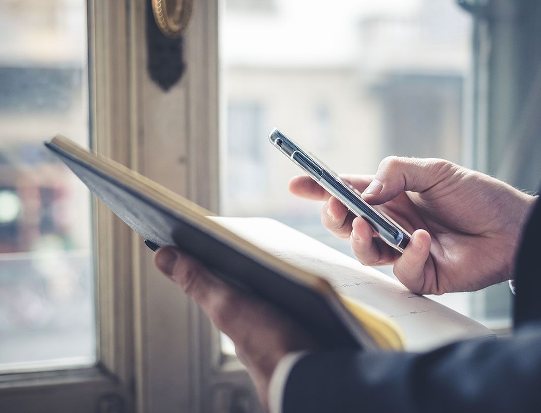 Hands holding a tablet and smartphone by a window, checking information on both devices