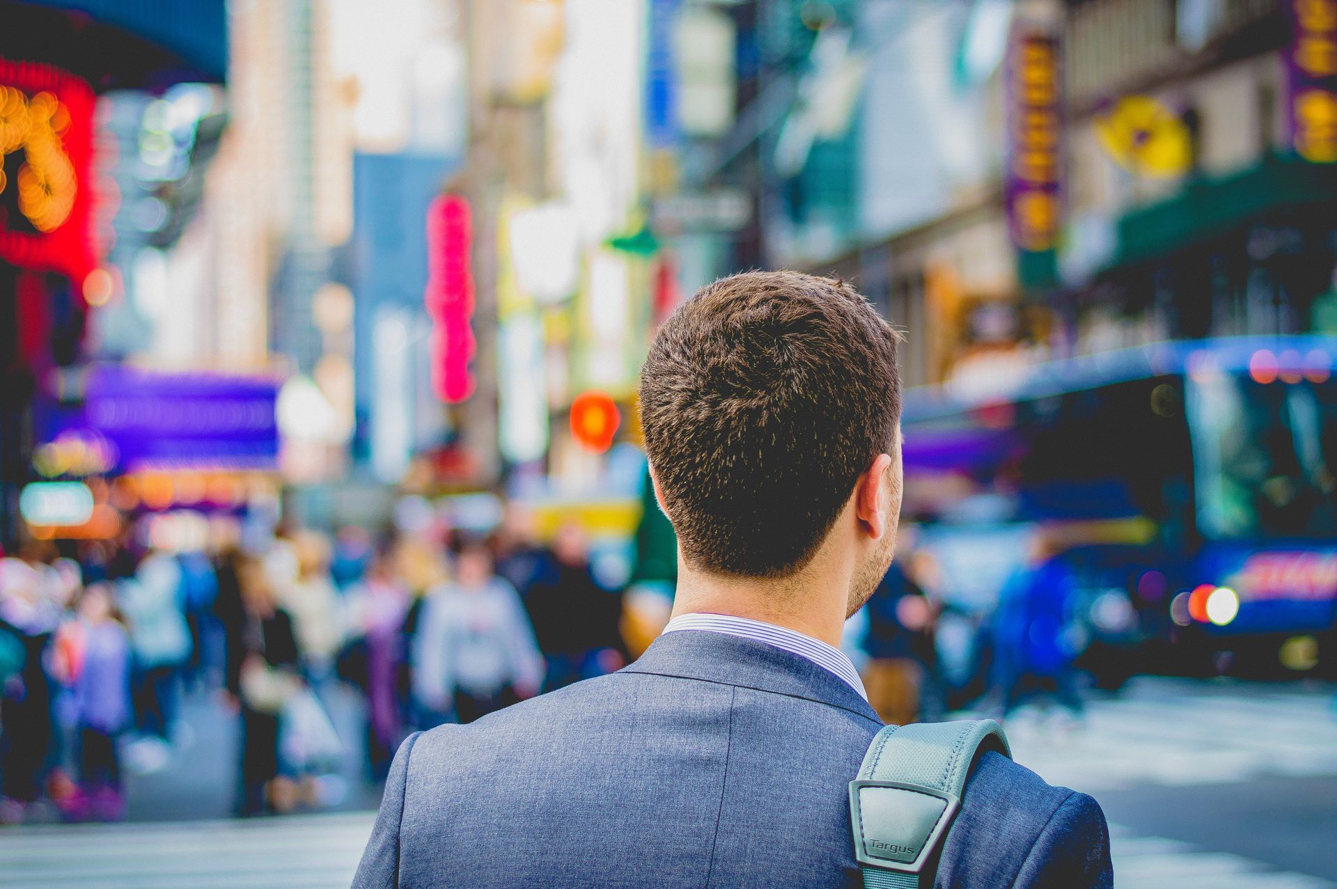 Person seen from behind crossing a busy city street with colorful neon signs and blurred traffic.