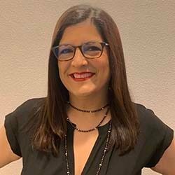 Smiling woman with glasses and dark hair wearing a black top against a beige background