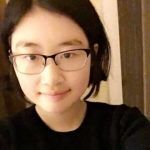 Person with glasses and short dark hair smiling in a softly lit indoor setting