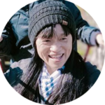 Smiling person in a black knit hat and scarf, outdoors in a snowy scene