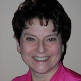 Close-up portrait of a smiling person with short dark hair on a plain light background