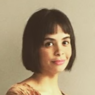 Portrait of a woman with a short dark bob, wearing a patterned top, against a plain beige background