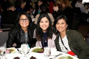 Three people smiling at a table in a restaurant, with plates and drinks in front of them.