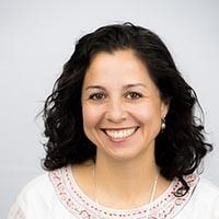 Smiling woman with curly dark hair wearing a white top against a light background