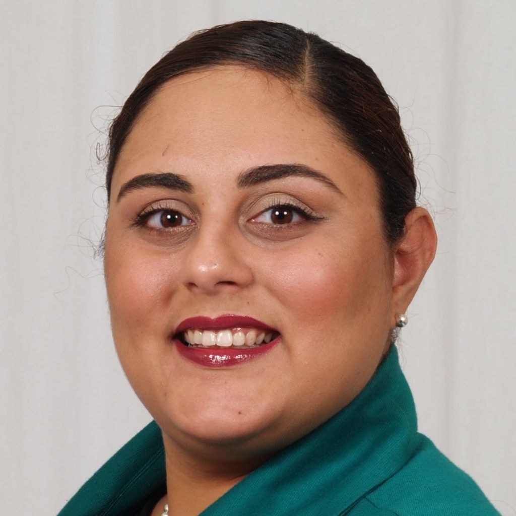 Portrait of a smiling woman in a teal jacket against a light background