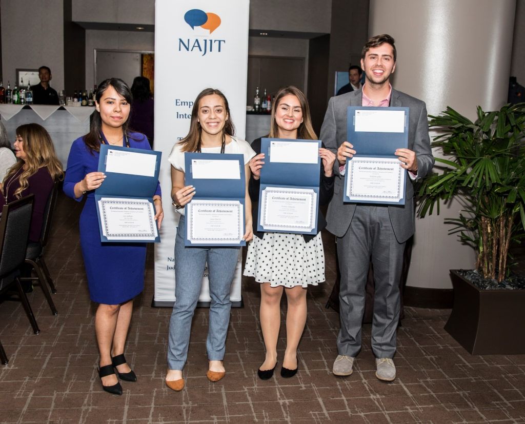 Four people holding framed certificates in front of a NAIJ sign at an awards event.