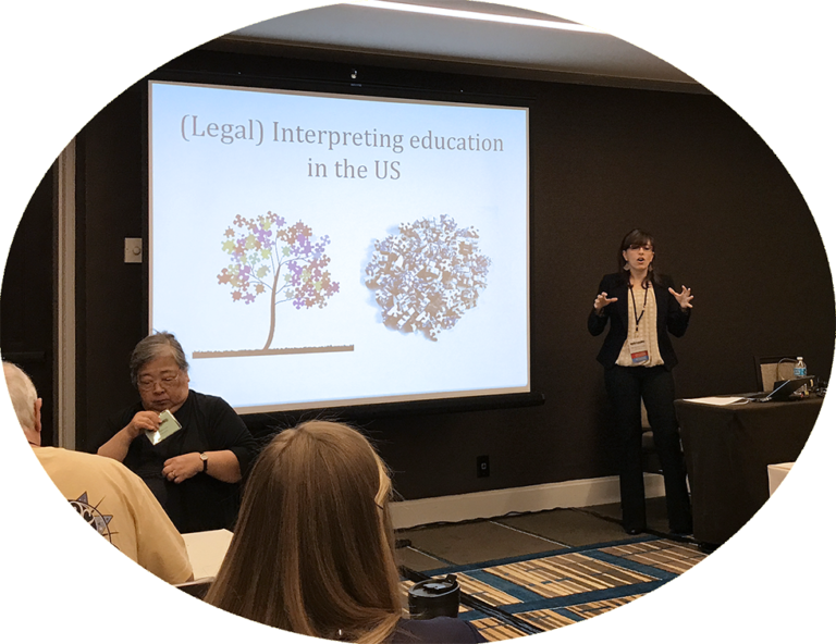 Presenter speaks beside slide titled “(Legal) Interpreting education in the US” in a conference room.