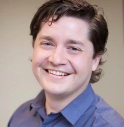 Smiling person in a blue shirt against a neutral background