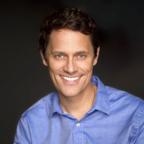 Smiling man in a blue shirt against a dark background