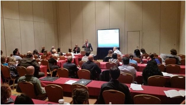Conference room with seated audience facing a speaker and projected presentation screen
