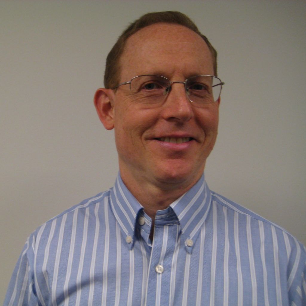 Smiling man in glasses wearing a blue striped button-down shirt against a plain background