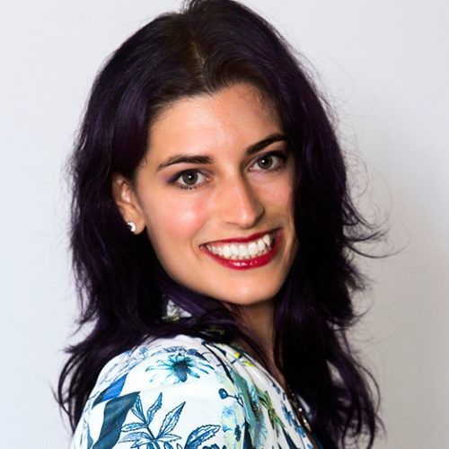 Smiling woman with dark hair wearing a white floral top against a light background