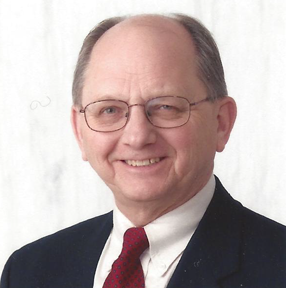 Portrait of a smiling man in glasses, dark suit, white shirt, and red tie against a light background