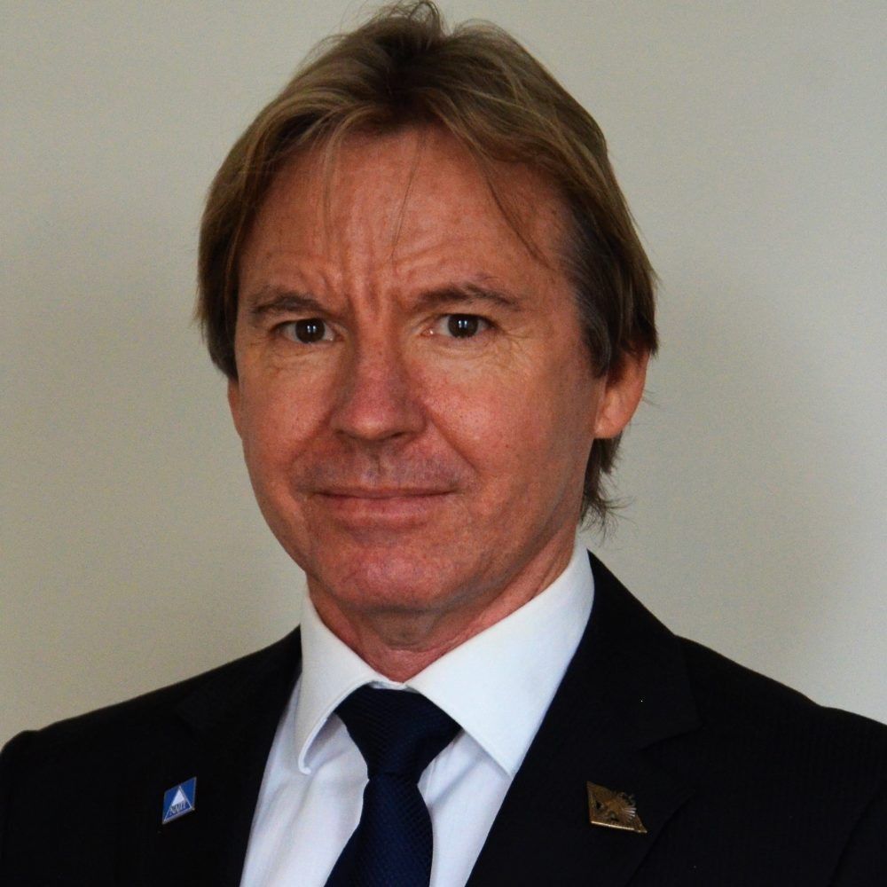 Man in a dark suit and navy tie, posed against a plain light background.