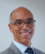 Smiling bald man in glasses and a suit against a light gray background
