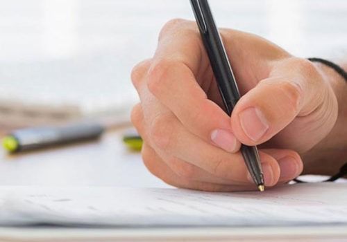 Close-up of a hand writing with a black pen on paper
