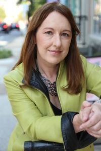 Woman in a lime green jacket sitting outdoors, looking at the camera.