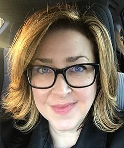 Close-up portrait of a person wearing black glasses and a black top, seated in a car.