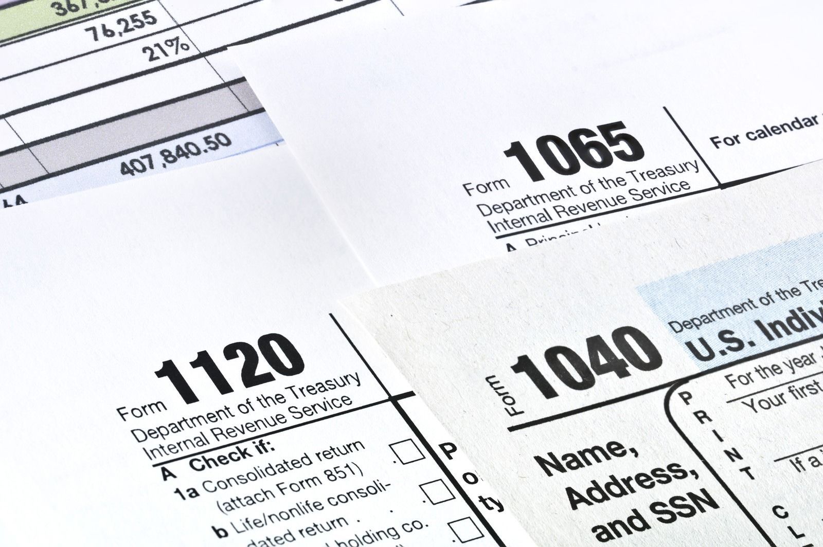 Scattered U.S. tax forms, including 1040, 1120, and 1065, on a white surface.
