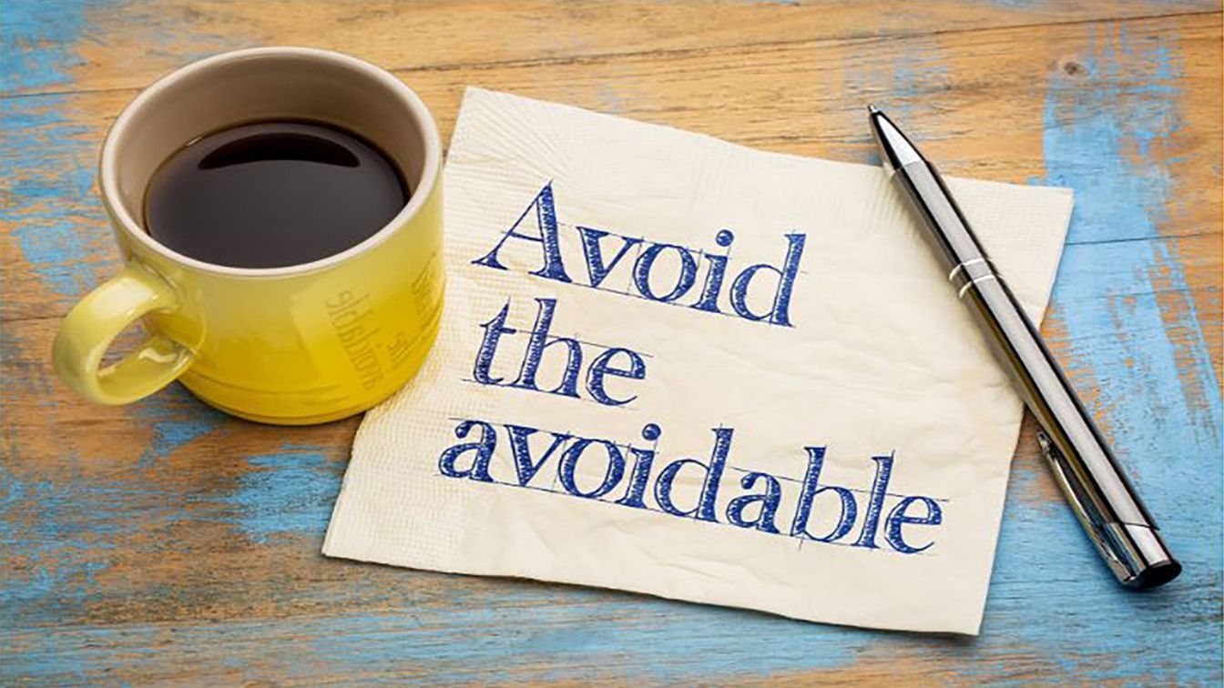 Coffee cup, pen, and note reading “Avoid the avoidable” on a weathered blue table.