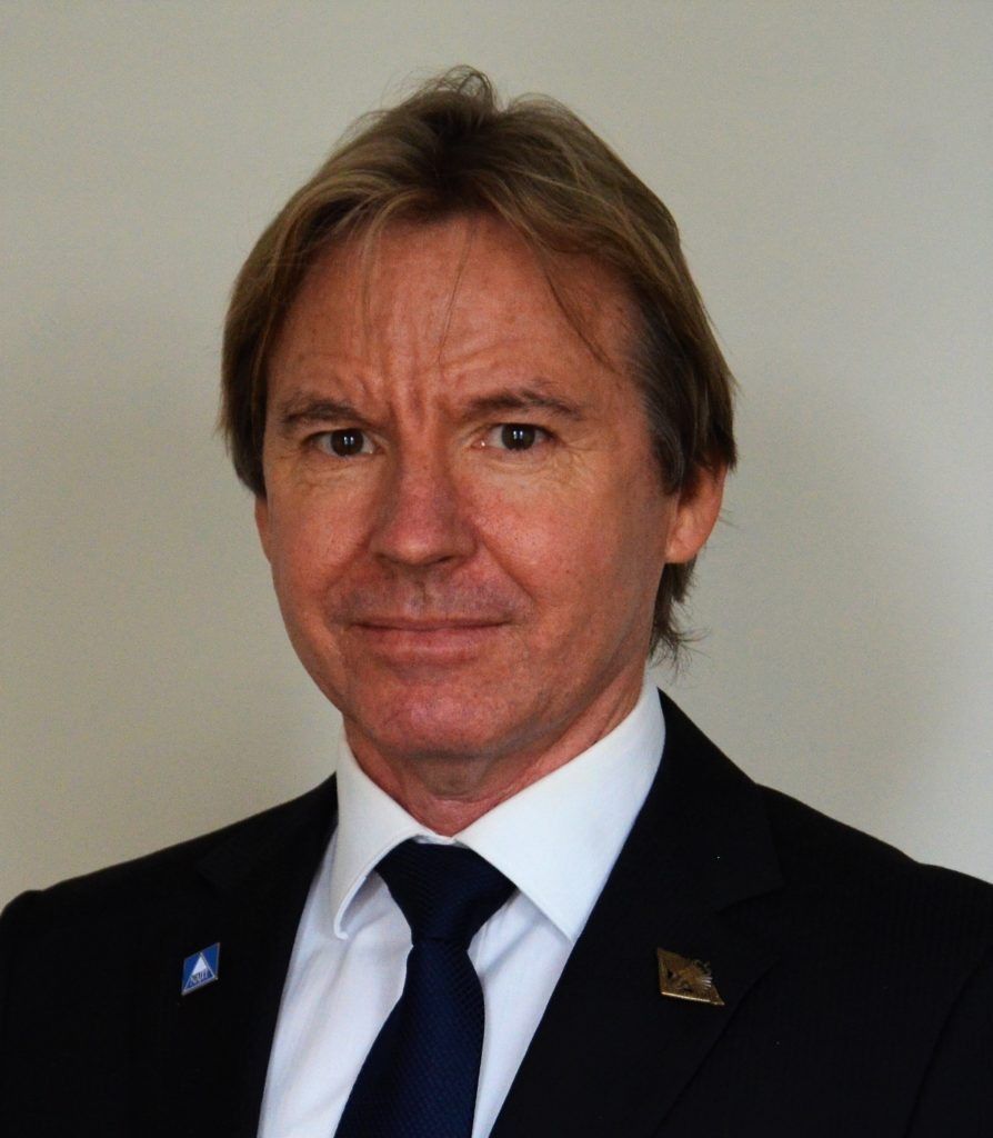 Man in a dark suit and tie, facing the camera against a plain light background.