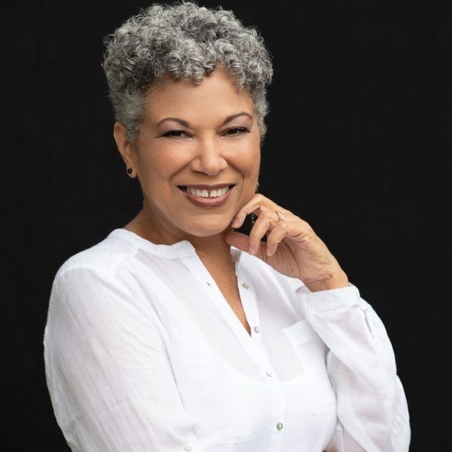 Smiling person in a white blouse, posed against a dark background.