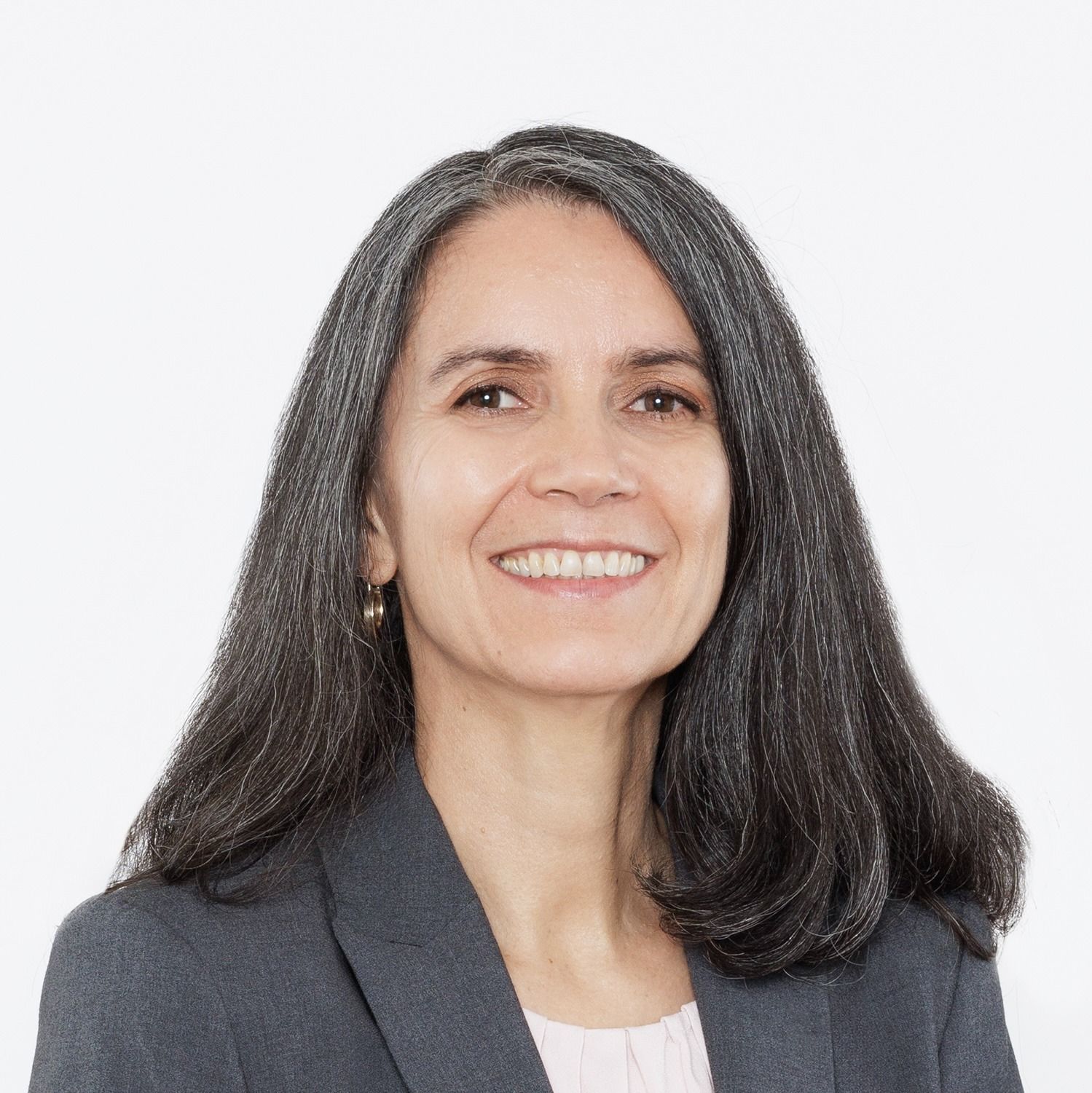 Smiling woman with long dark hair wearing a gray blazer on a white background