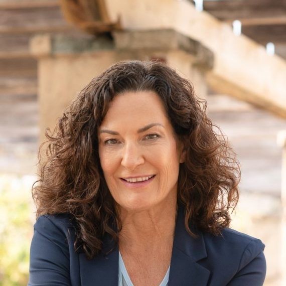 Smiling woman with curly dark hair in a navy blazer, outdoors in front of stone steps
