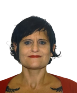 Portrait of a person with short dark hair, red top, and tattoos on both shoulders against a white background