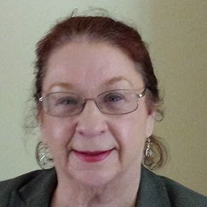 Portrait of a woman wearing glasses and earrings, smiling against a plain light background