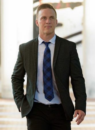 Man in a dark suit and blue tie walking indoors with hands in pockets