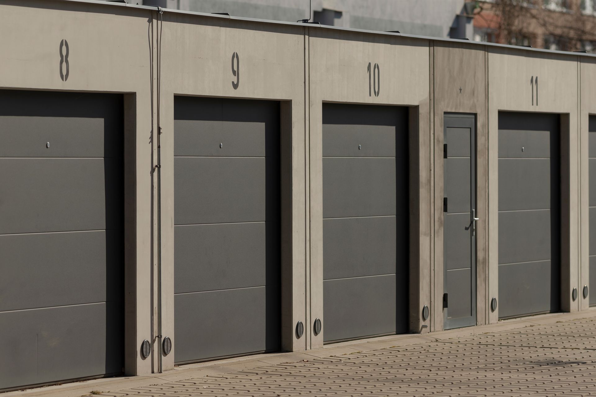 Row of gray storage unit doors along a beige building on a gravel lot