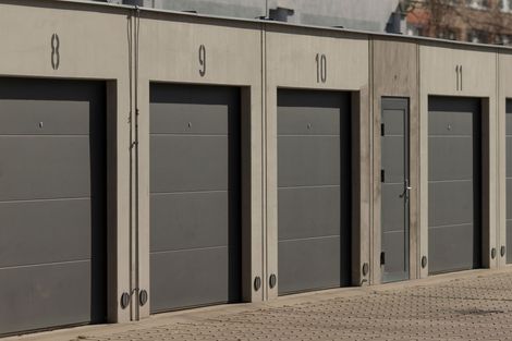 Rangée de portes de garage industrielles grises sur un bâtiment beige dans un terrain pavé