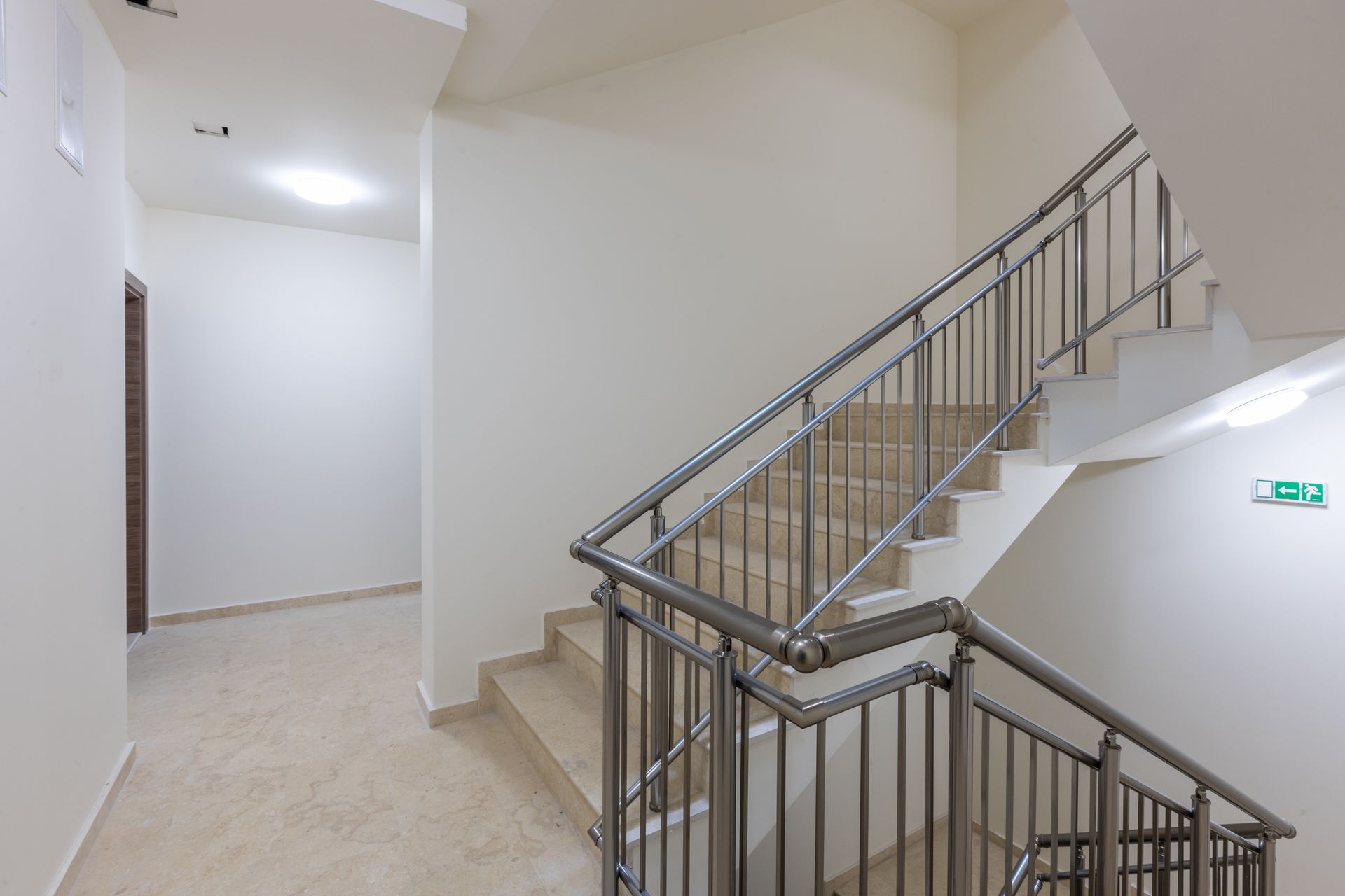Cage d'escalier intérieure vide avec sol carrelé beige et rampes métalliques sur murs blancs