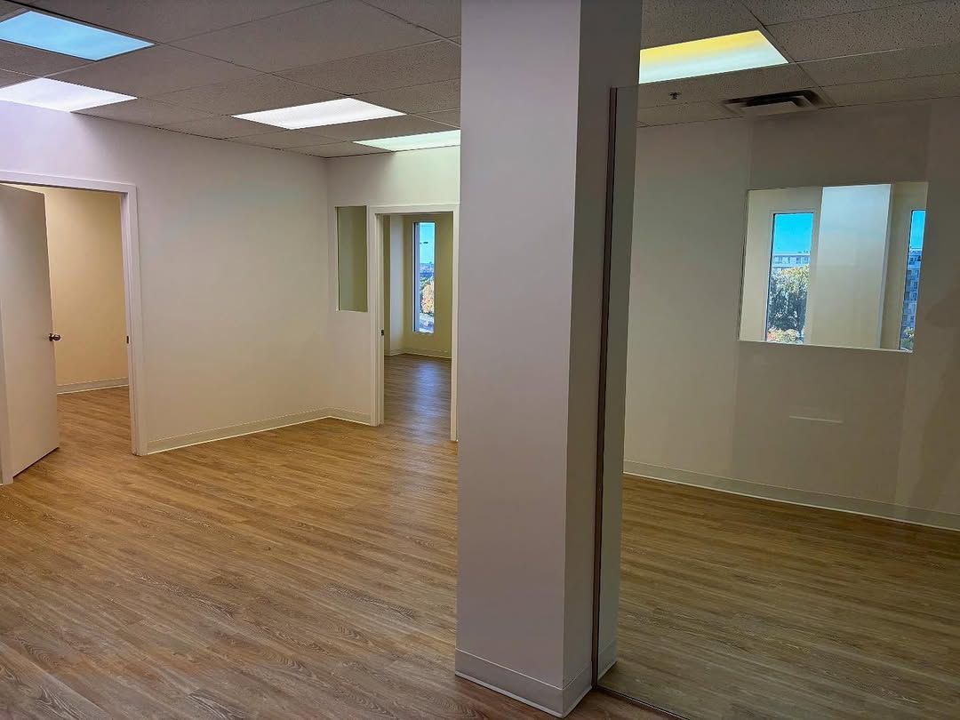 Espace de bureau vide avec parquet, murs blancs, éclairage au plafond et panneau mural en miroir.