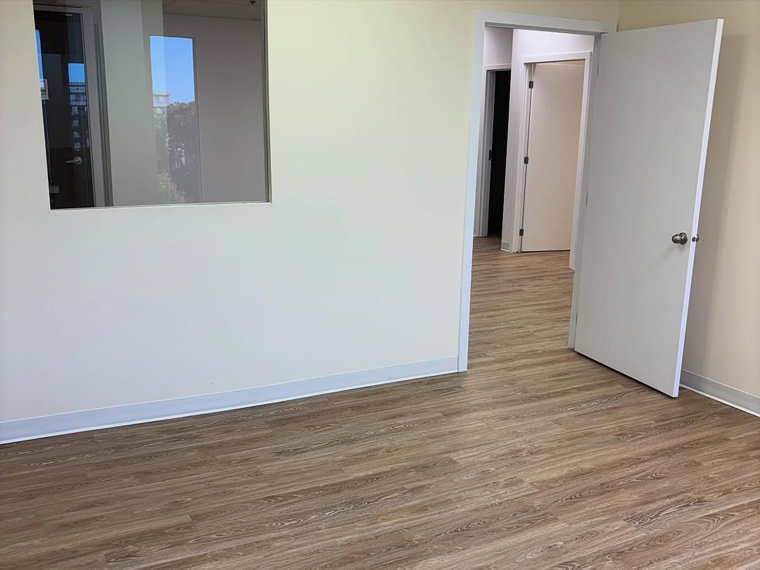Pièce vide avec parquet, murs blancs et une porte ouverte près d'un miroir mural.