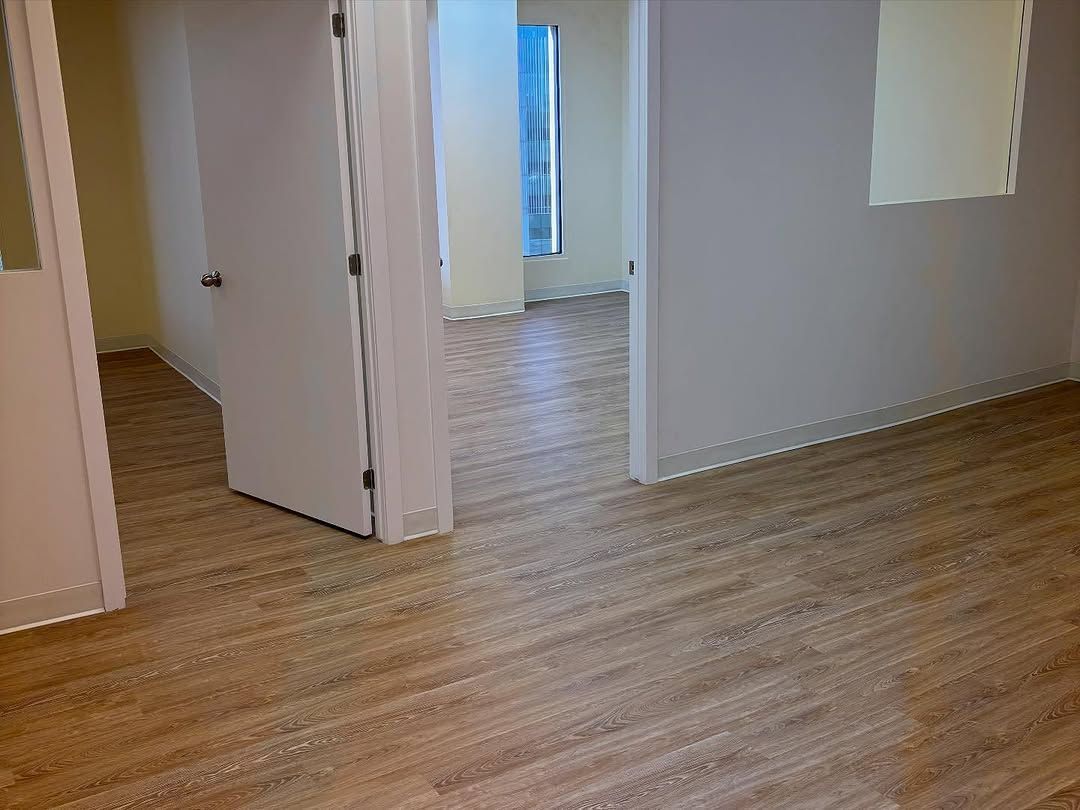 Pièce vide avec parquet clair et murs blancs, vue à travers une porte ouverte.