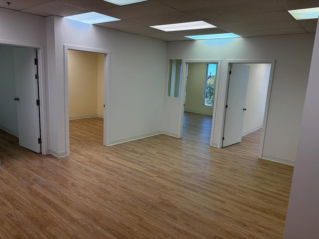 Espace de bureau vide avec parquet, murs blancs et portes ouvertes sous éclairage au plafond