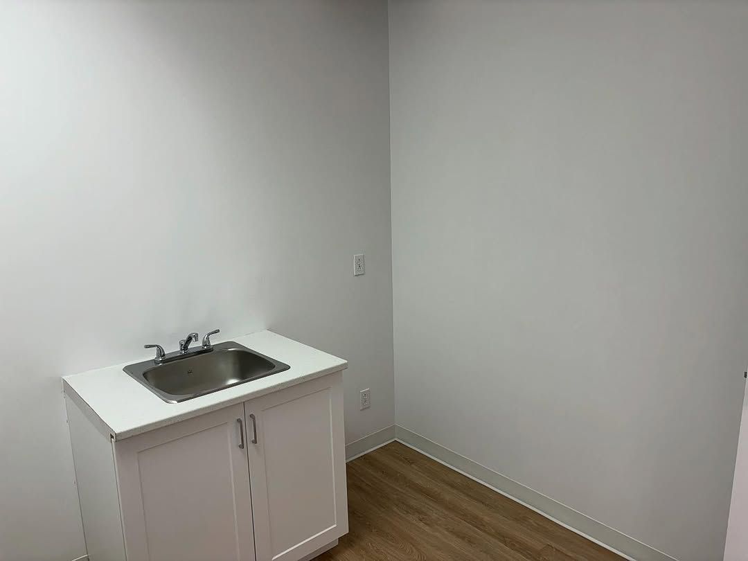 Petite pièce vide avec un meuble-lavabo blanc contre le mur et un sol en bois.