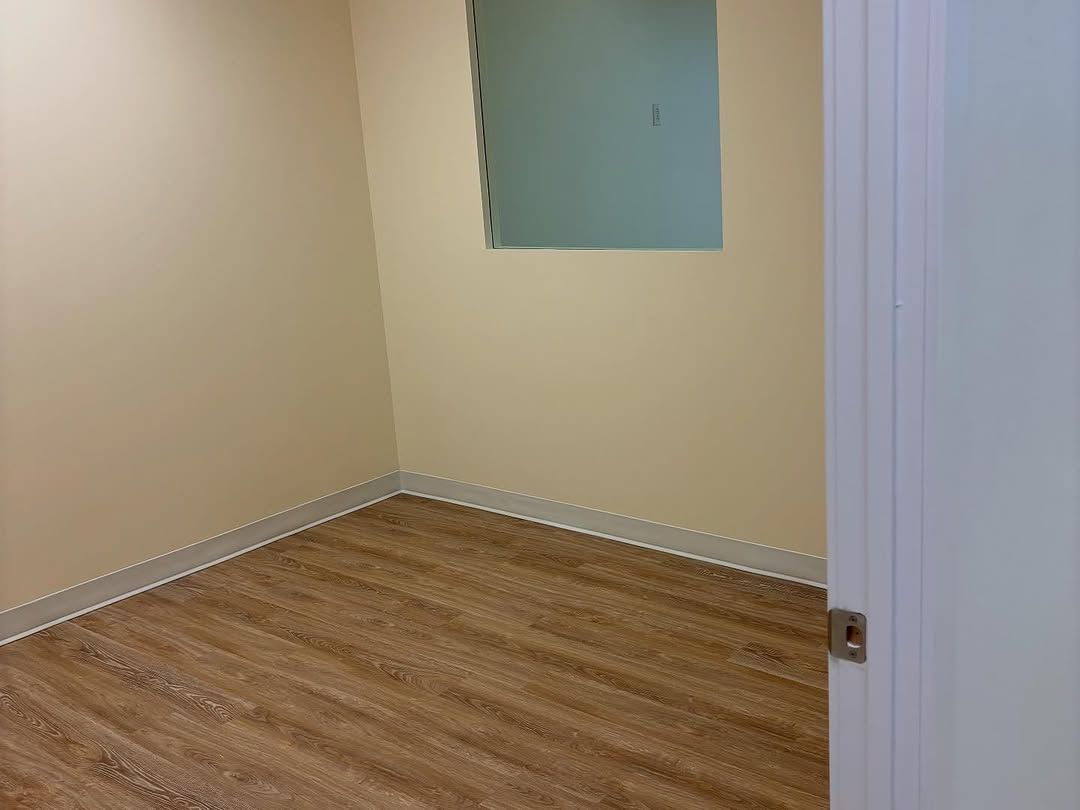 Pièce beige vide avec parquet et une petite niche dans le mur, vue à travers une porte blanche entrouverte.