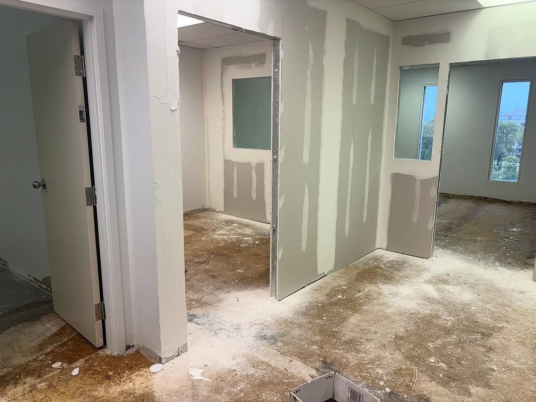 Intérieur inachevé avec cloisons sèches, portes ouvertes et sols jonchés de débris dans un couloir de pièce rénové.