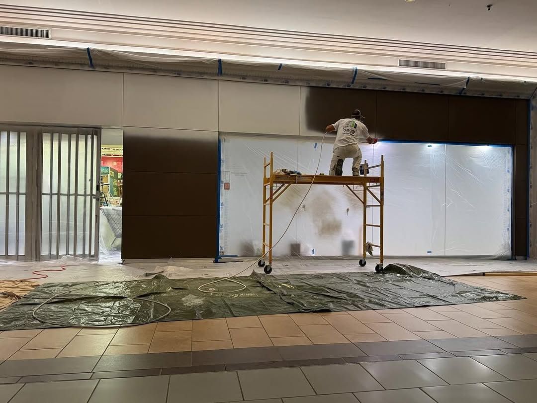 Un homme, juché sur un échafaudage, peint un mur dans une cour intérieure recouverte de bâches et de carrelage.