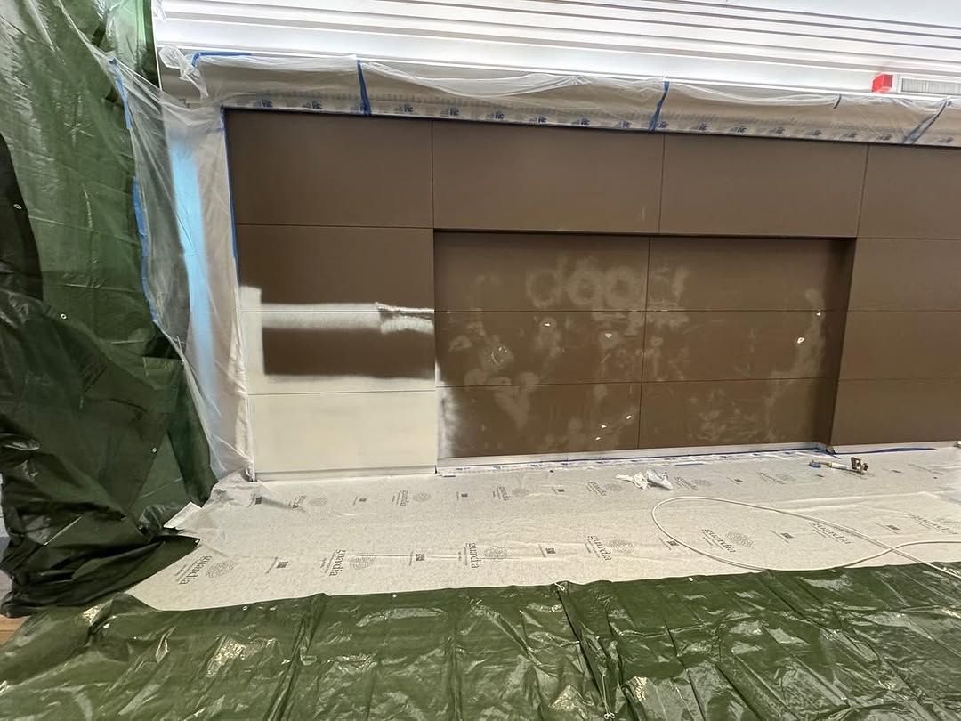 Façade de magasin partiellement peinte, avec une porte de garage marron et une bâche verte à gauche, entourées de toiles de protection blanches.