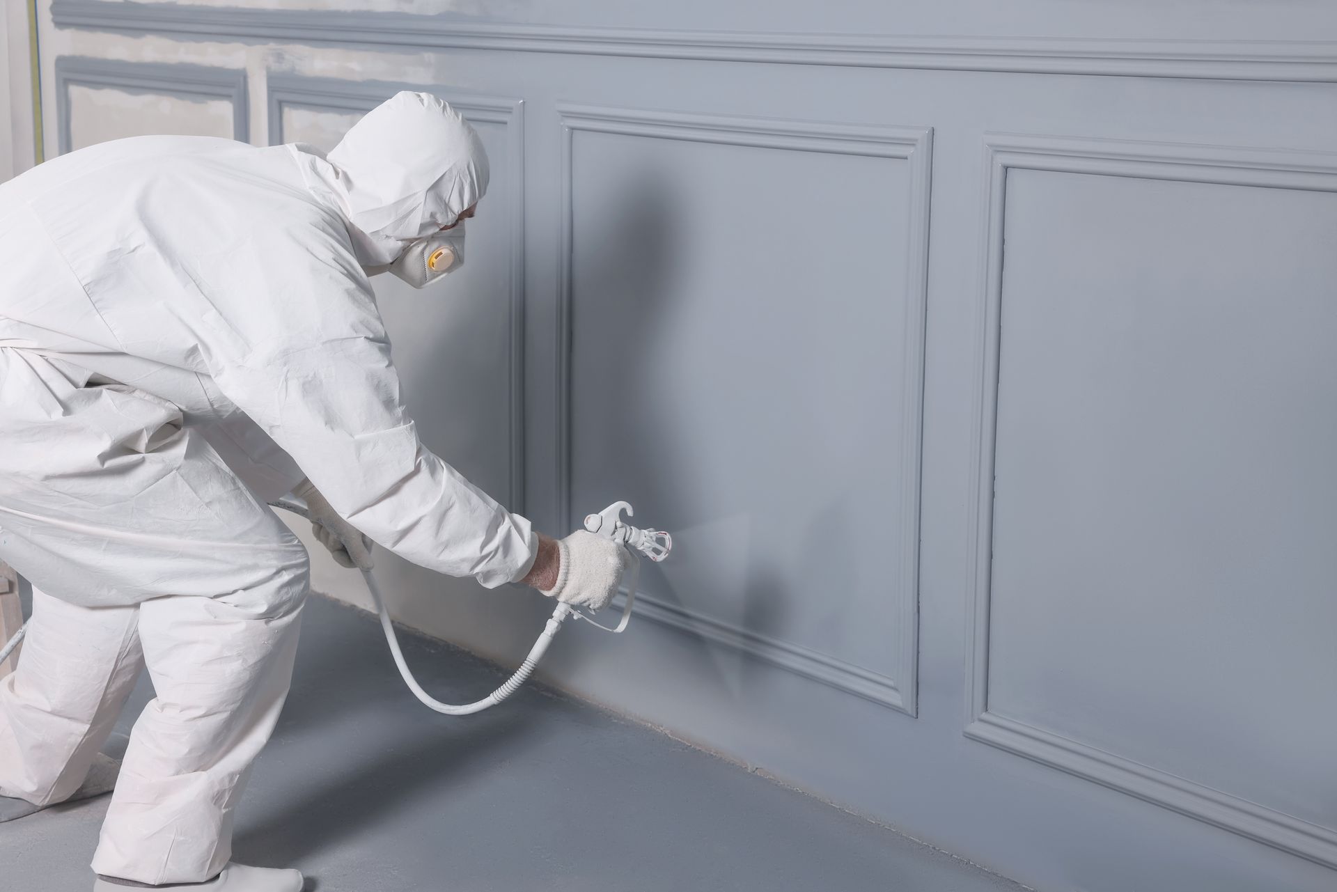 Un ouvrier en combinaison de protection blanche peint un mur au pistolet à peinture.