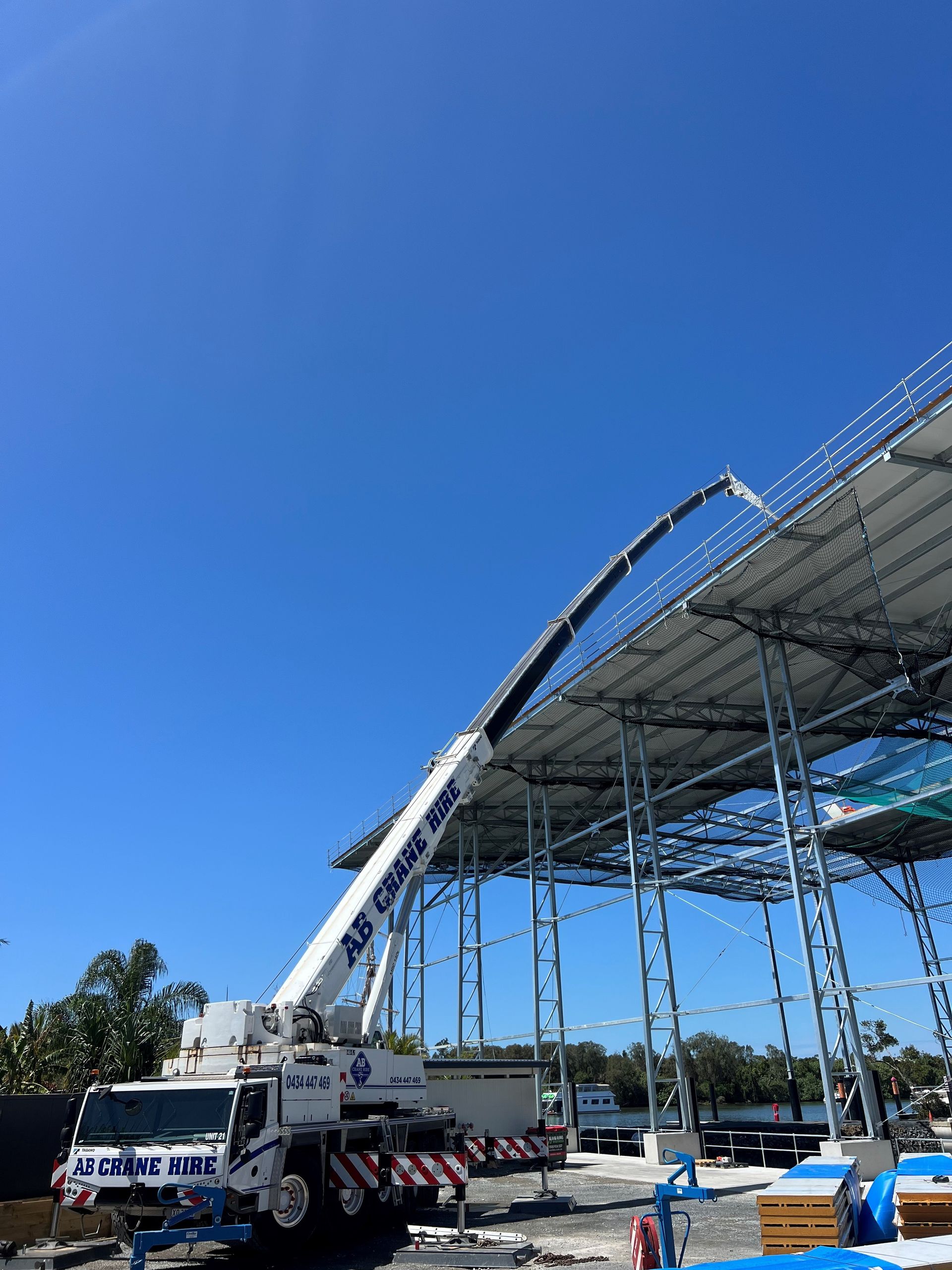 Truck-mounted crane lifting steel trusses at an outdoor construction site under a clear blue sky