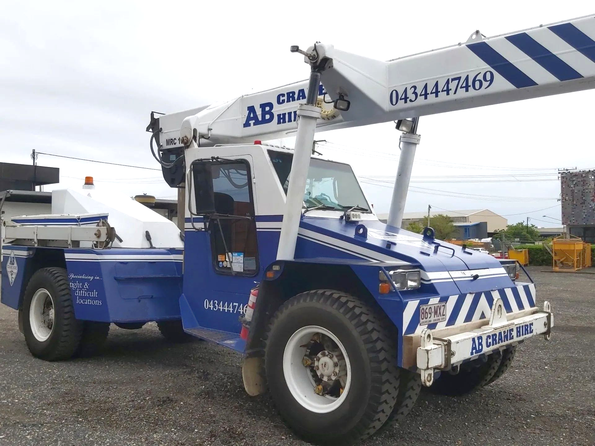 Blue-and-white tow truck parked on gravel, with a crane arm and company signage.