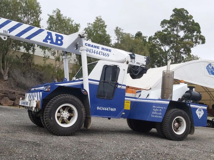 Blue-and-white cement mixer truck on a gravel site near trees and a concrete structure