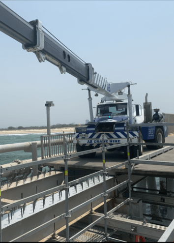 Utility truck with extended crane on a rooftop platform by the water under a clear sky
